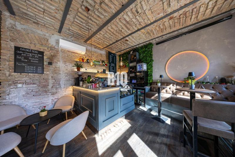 Innenraum eines Gastronomiebereichs mit Bartresen, Ziegelwänden und einem Boden in Holzoptik.