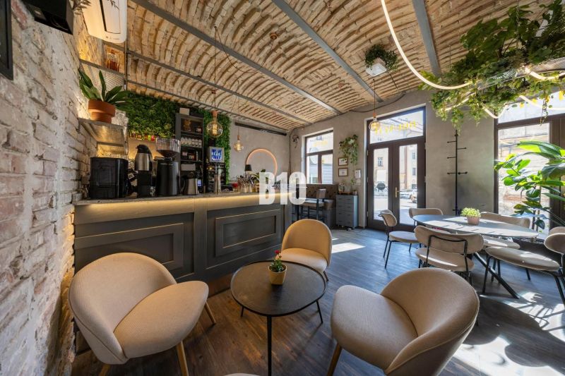 Ein Interieur mit einer von Pflanzen umgebenen Bar, einem Boden mit Holzdekor und einer gemütlichen Sitzgelegenheit.