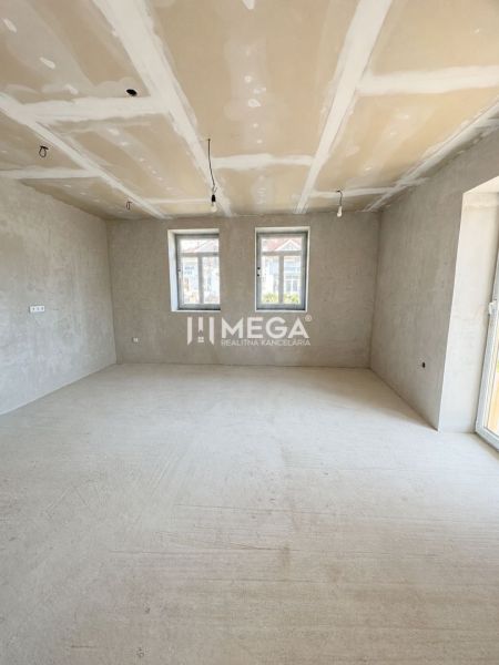 Ein geräumiges Zimmer in einem Einfamilienhaus mit großen Fenstern und Betonboden.