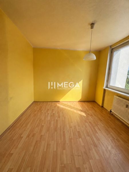 Gelbes Zimmer mit großem Fenster und Holzboden in einer 3-Zimmer-Wohnung.