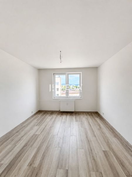 Ein heller, leerer Raum mit weißen Wänden und einem Boden in Holzoptik in einer 2-Zimmer-Wohnung.