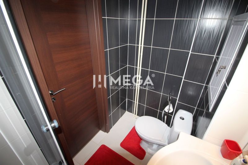 Badezimmer in der Ferienwohnung mit Dusche, Toilette und schwarzen Fliesen.