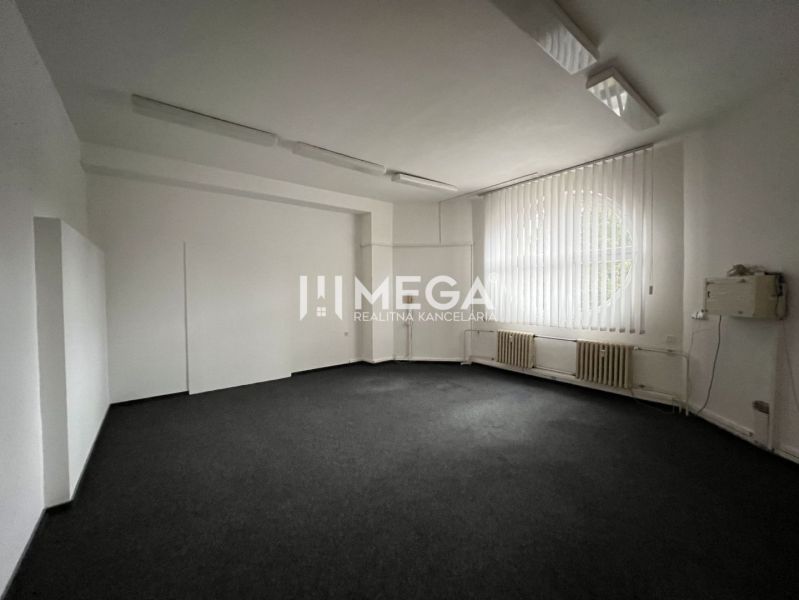 Büroflächen mit Teppichboden, großem Fenster und vertikalen Jalousien.