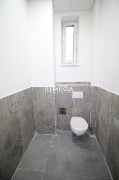 Ein Badezimmer in Geschäftsräumen mit einfachem Design verfügt über eine Toilette und ein schmales Fenster.