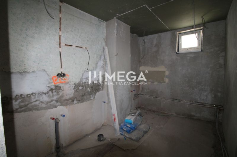 Nedokončená miestnosť v rodinnom dome s nedokončenými stenami a stavebným materiálom.