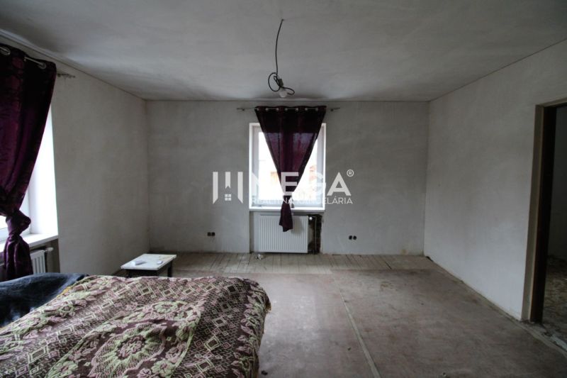 Schlafzimmer in einem Einfamilienhaus mit abblätterndem Boden und lila Vorhängen.