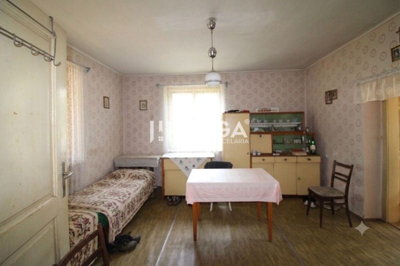Ein Zimmer in einem Einfamilienhaus mit Tapeten, einem Tisch, einem Bett, einer Vitrine und einem Boden mit Holzdekor.