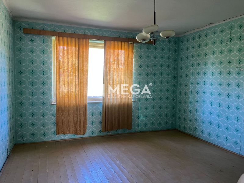 Ein Zimmer in einem Einfamilienhaus mit gemusterten Tapeten und einem Boden in Holzoptik.