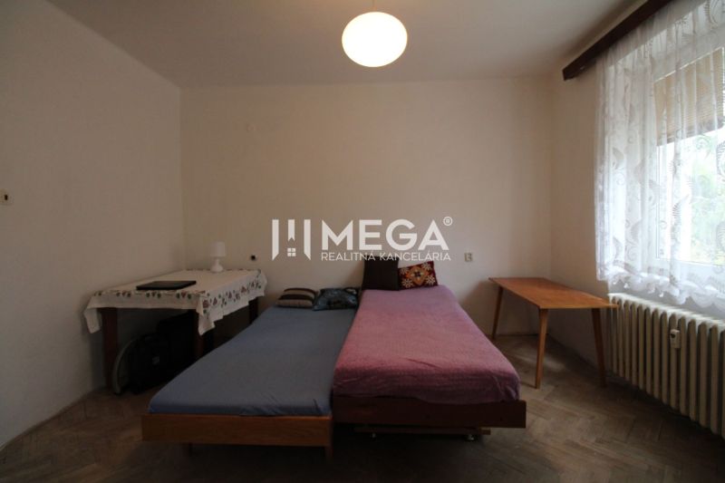 Schlafzimmer in einer 2-Zimmer-Wohnung mit Bett, Tisch und Boden in Holzoptik.