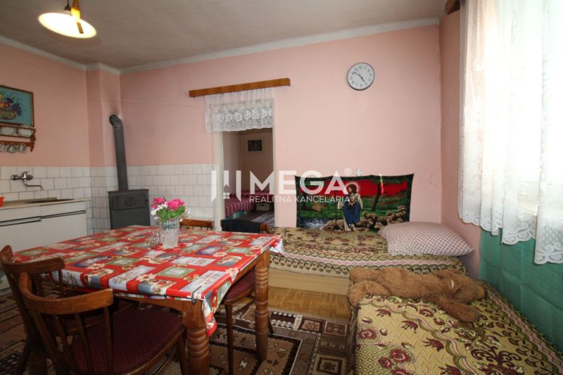 Innenraum eines Einfamilienhauses mit Küchentisch, Kachelofen und Bett, Boden mit Holzdekor.