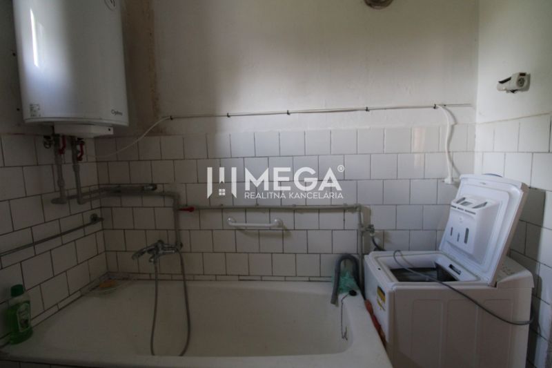 Ein Badezimmer in einem Einfamilienhaus mit einer Badewanne und einer Waschmaschine, umgeben von weißen Fliesen.