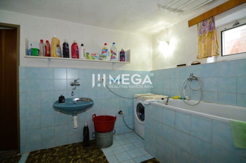Ein Badezimmer in einem Einfamilienhaus mit Badewanne, Waschbecken und Waschmaschine, ausgestellte Reinigungsmittel.