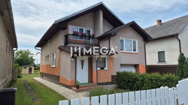 Ein Einfamilienhaus in Lackovce mit Balkon, umgebender Vegetation und einem weißen Zaun.