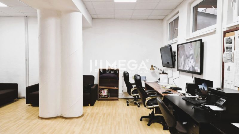 Ein Büro mit einem Boden in Holzoptik, Tischen, Stühlen und Bildschirmen an der Wand.