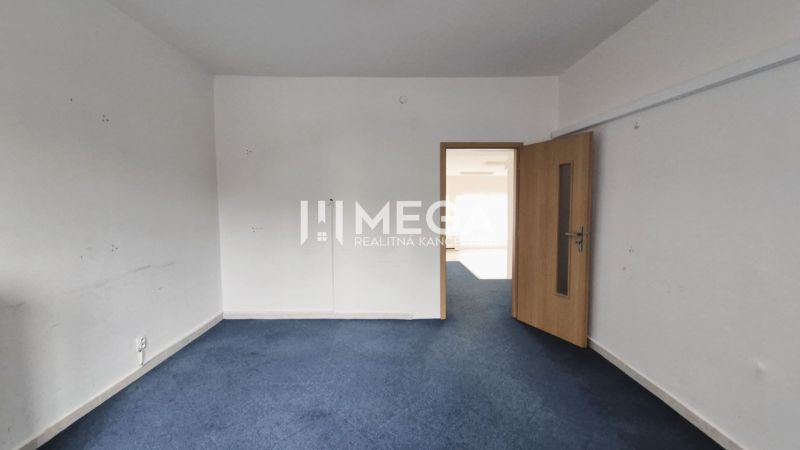 Geschäftsräume mit blauem Teppichboden und heller Wand, geschlossene Holztür.