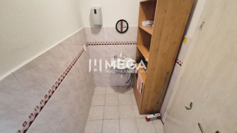 Badezimmer in Geschäftsräumen mit Waschbecken, Regalen und Fliesen an den Wänden.
