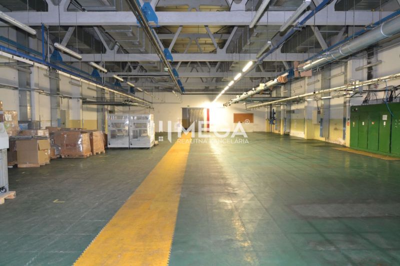 Produktionsräume mit Betonboden und Beleuchtung, Lagerung von Materialien auf Paletten.