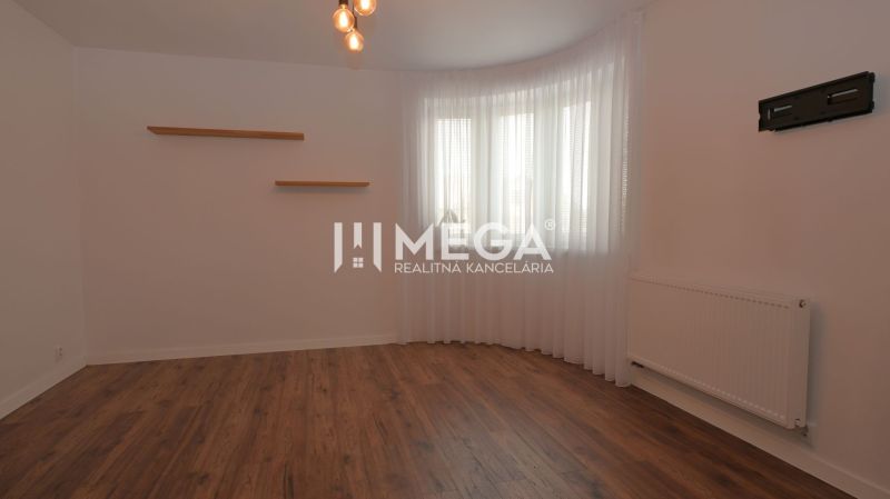 Ein Zimmer in einem Einfamilienhaus mit einem Boden in Holzoptik, weißen Wänden und Vorhängen.