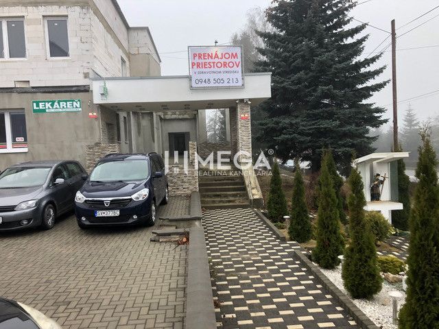 Gebäude in der SNP-Straße in Snina mit Parkplatz und Werbung für die Vermietung von Räumlichkeiten.