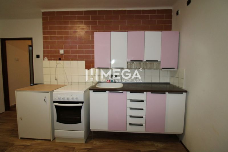 Küche in einer 2-Zimmer-Wohnung mit rosa Schränken und einem Boden in Holzoptik.