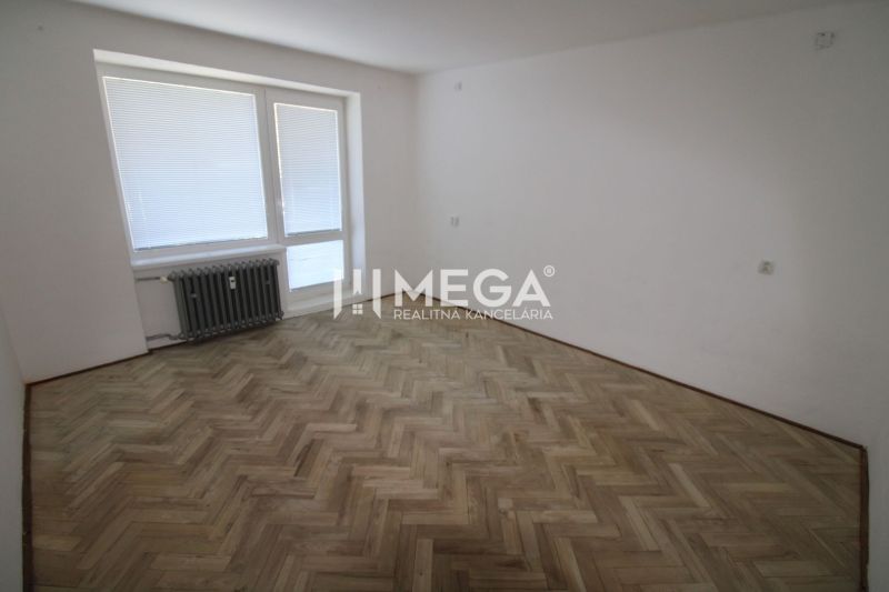 Ein geräumiges Zimmer in einer 2-Zimmer-Wohnung mit einem Boden in Holzoptik und einem Heizkörper.