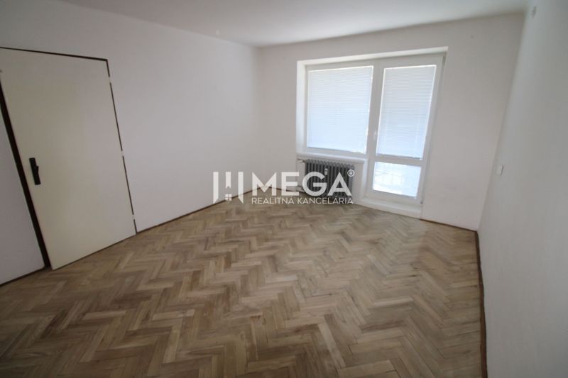 Ein Zimmer mit Fenster und Holzboden in einer Zweizimmerwohnung.