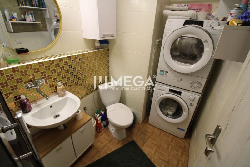 Badezimmer in einer 2-Zimmer-Wohnung mit Waschmaschine und Trockner, Fliesen mit Holzdekor.
