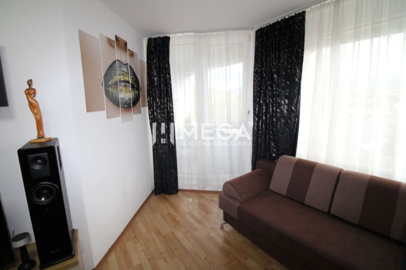 Wohnzimmer in einer 2-Zimmer-Wohnung mit dunklem Sofa, Lautsprecher und Boden in Holzoptik.