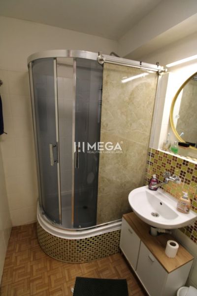 Badezimmer in einer 2-Zimmer-Wohnung mit Holzboden, Duschkabine und Waschbecken.