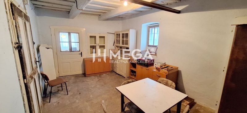 Ein Zimmer in einem Einfamilienhaus mit älteren Möbeln und einem Tisch, ohne dekorativen Bodenbelag.
