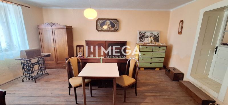 Ein Zimmer in einem Einfamilienhaus mit einem Boden in Holzoptik, einem Tisch, Stühlen und antiken Möbeln.