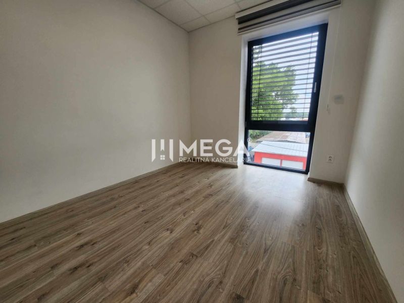 Ein Büro mit einem Boden in Holzoptik und einem großen Fenster, schlichtes Interieur.