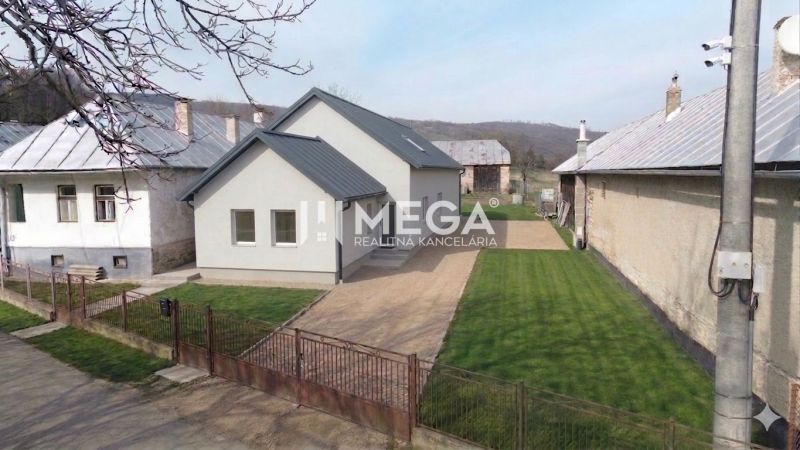 Ein Einfamilienhaus in Zbojná mit Rasen und grauem Dach zwischen zwei benachbarten Gebäuden.