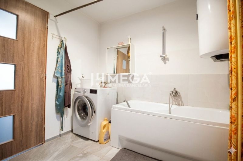 Badezimmer in einem Einfamilienhaus mit Waschmaschine, Badewanne, Spiegel und Vorhang.