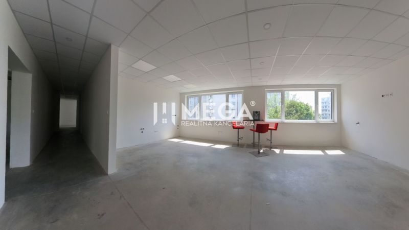 Ein klares Büro mit weißen Wänden, Deckenplatten und roten Stühlen bei den Fenstern.