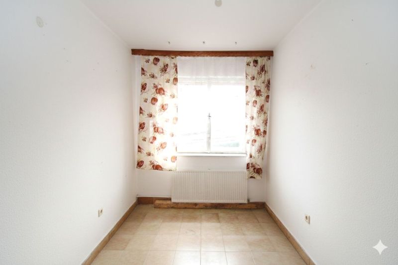 Ein Zimmer in einem Einfamilienhaus mit Fenster, Blumen-Vorhängen und Fliesen.