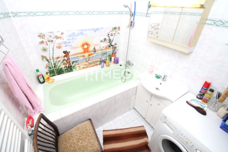 Badezimmer mit grüner Badewanne und Waschmaschine in einem Einfamilienhaus, Dekor tropischer Landschaft auf den Fliesen.