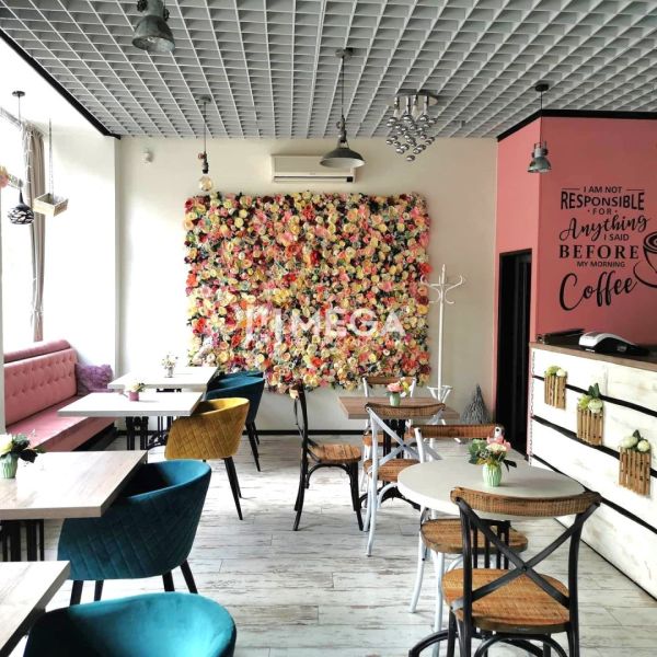 Ein Café mit einer Blumenwand in gastronomischen Räumlichkeiten und Stühlen in verschiedenen Farben.