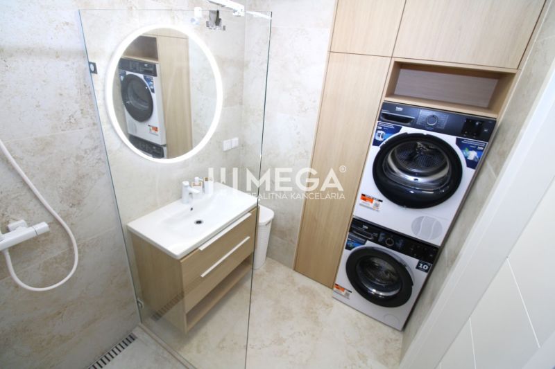 Badezimmer in einer 3-Zimmer-Wohnung mit Waschmaschine, Trockner und beleuchtetem rundem Spiegel.