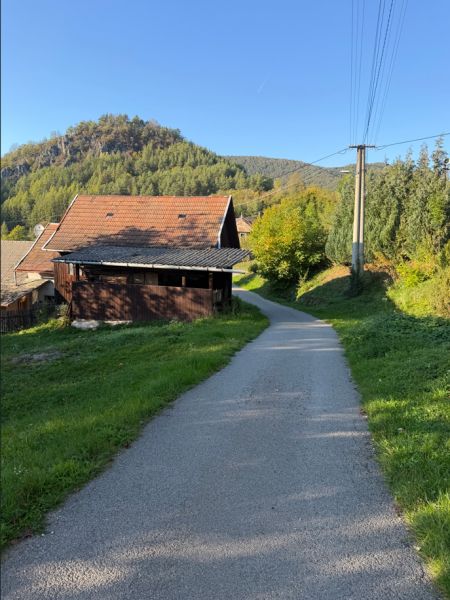 Die Straße in Košecké Podhradie führt an Häusern vorbei, gesäumt von Grün und Hügeln. Grundstücke - Wohnen.
