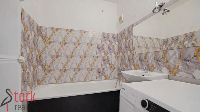 Badezimmer mit Badewanne und Waschmaschine in einer 3-Zimmer-Wohnung, Fliesen mit auffälligem Muster.