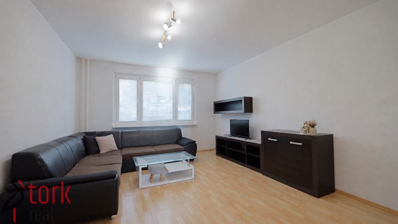 Wohnzimmer mit schwarzem Sofa, Schränken und Boden in Holzoptik, 3-Zimmer-Wohnung.
