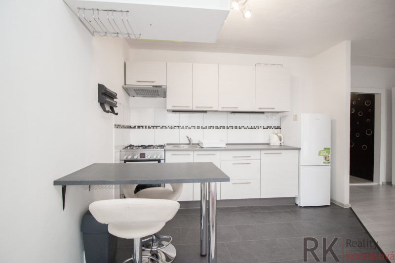 Küche in einer 2-Zimmer-Wohnung mit weißen Schränken und einem Esstresen.