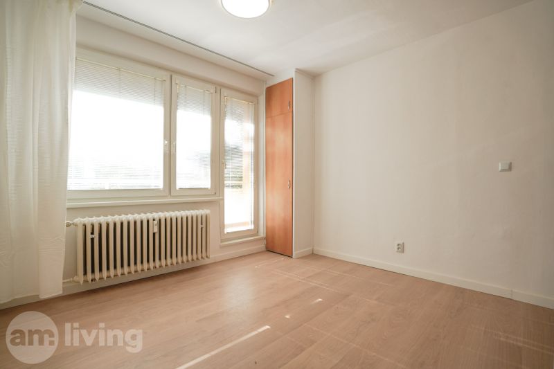 Ein Zimmer in einer Einzimmerwohnung mit einem Holzboden, weißen Wänden und Fenstern.
