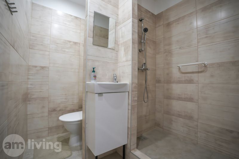 Badezimmer in einer Einzimmerwohnung mit Waschbecken, Dusche und beigen Fliesen.