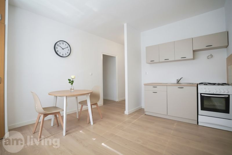 Küche in einer Einzimmerwohnung mit Holzboden, Esstisch und Uhr.