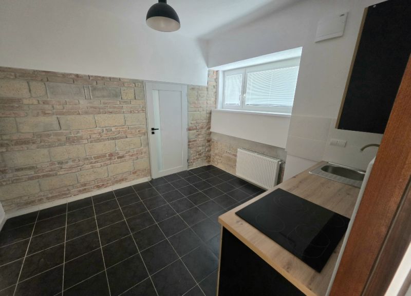 Küche in einer 2-Zimmer-Wohnung mit Ziegelverkleidung und schwarzem Fliesenboden.