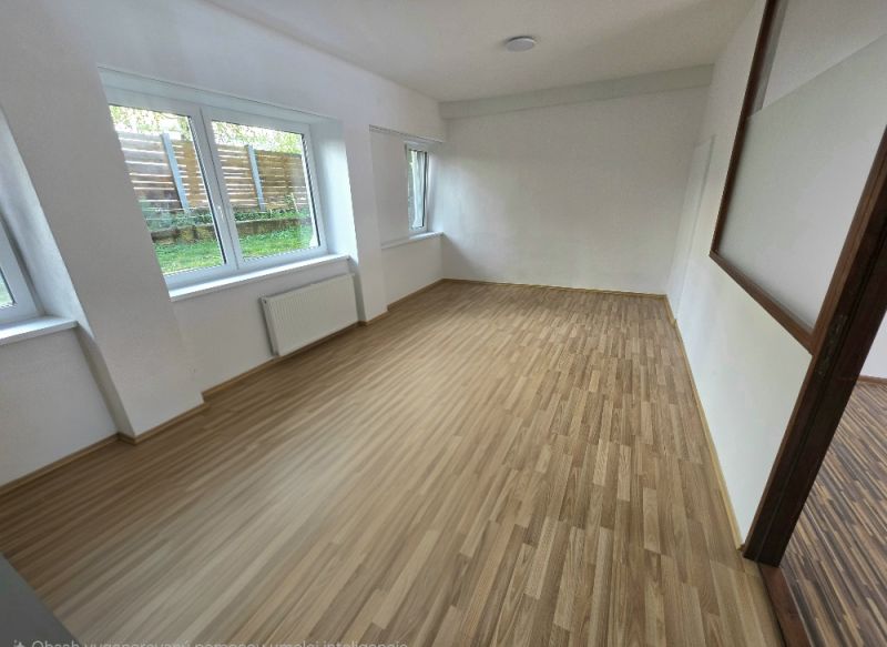 Ein Zimmer mit großen Fenstern und einem Holzboden in einer Zweizimmerwohnung.