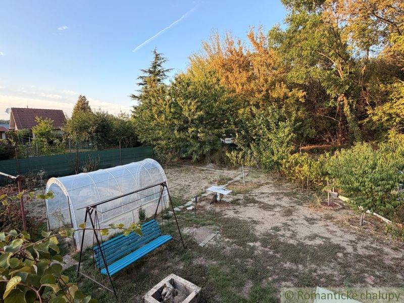 Der Garten bei der Hütte in Nové Zámky mit einer Schaukel und einem Folientunnel, umgeben von Grün.