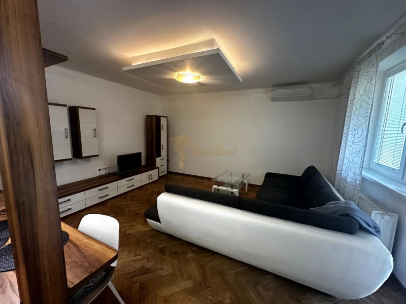 Wohnzimmer mit Sofa, Fernseher, Schränken und Holzboden in einer Zweizimmerwohnung.